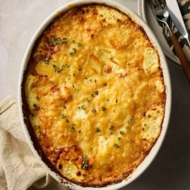 A cooked dish of Dauphinoise Potatoes on a table, with cutlery and napkins around it.