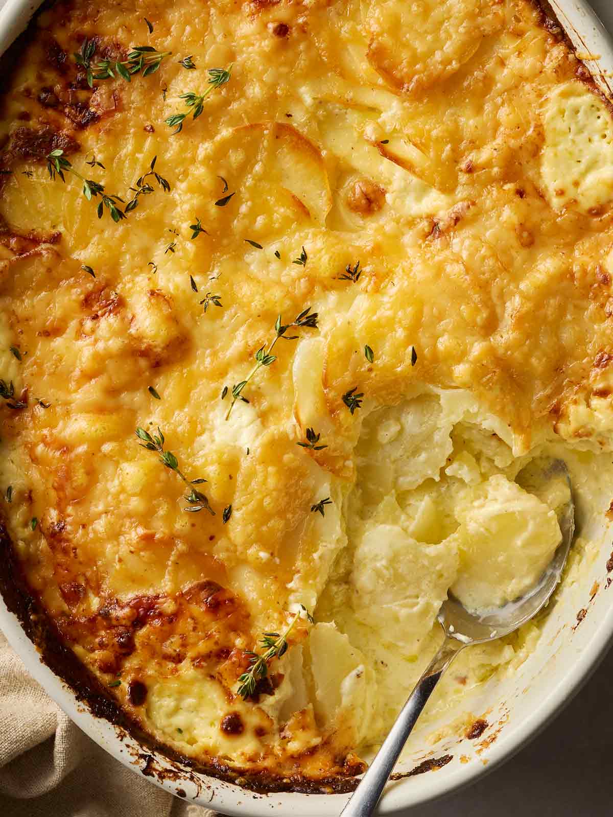 A close up of a dish of Dauphinoise Potatoes, with a spoon dishing up one portion.