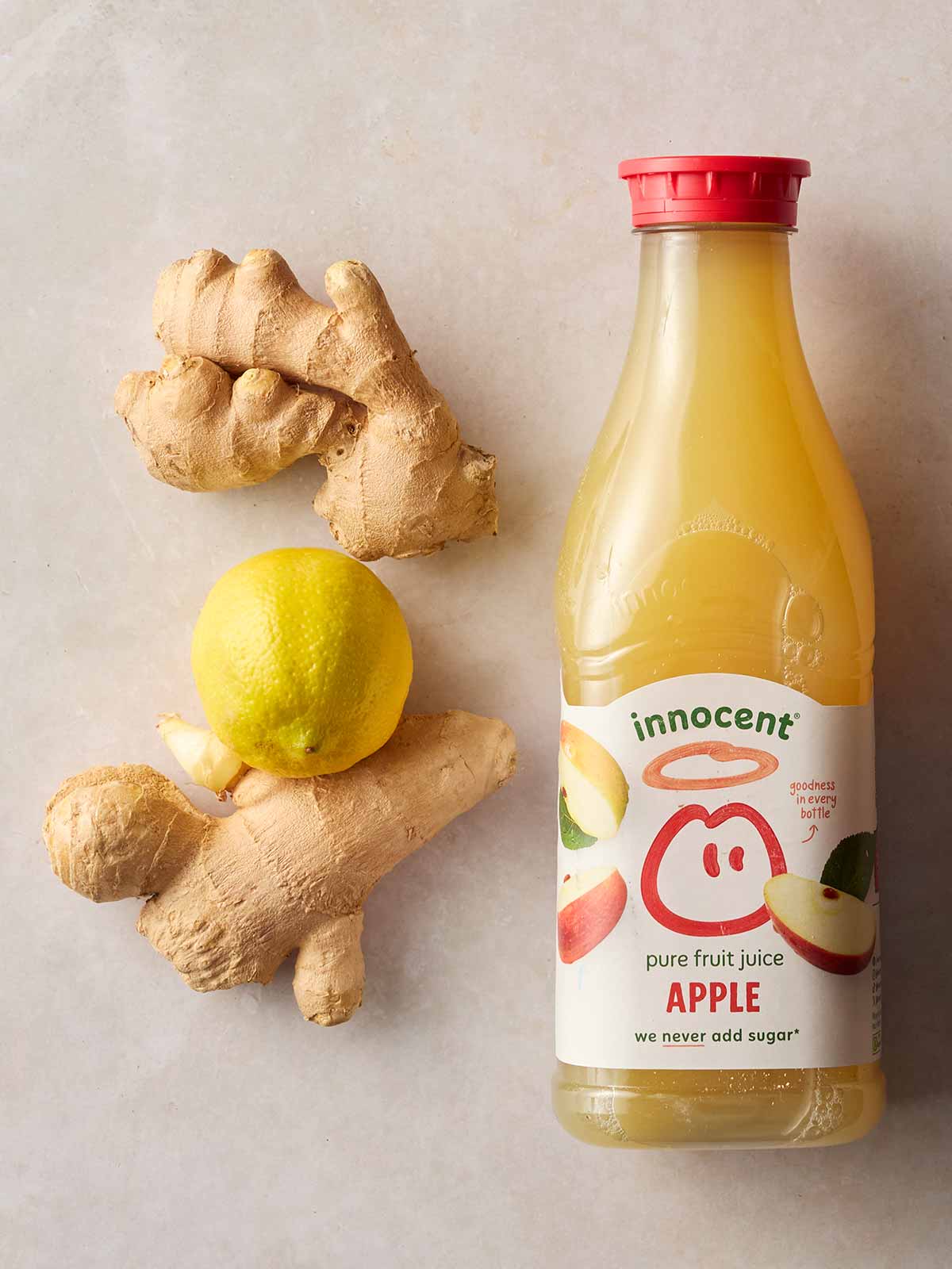 Ingredients laid out on a white surface, including a bottle of apple juice, fresh ginger and a lemon.