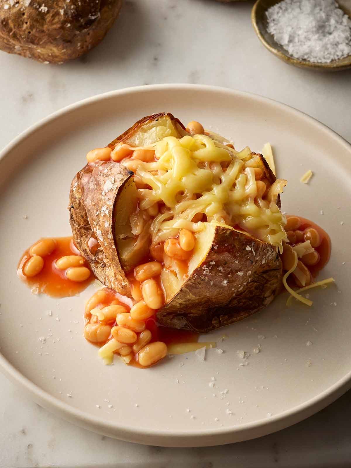 A plate with a jacket potato with beans and cheese on top.