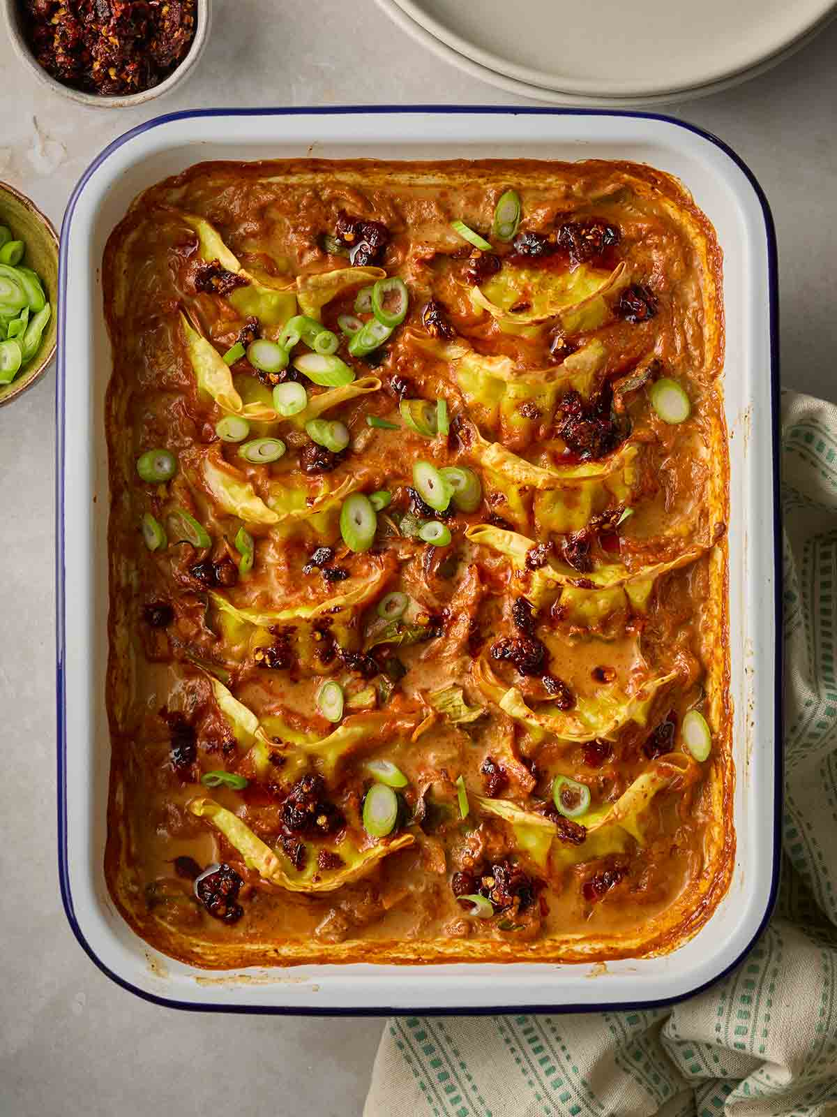 A pan of cooked Baked Dumplings in a stir fry sauce, ready to serve on a table with plates.