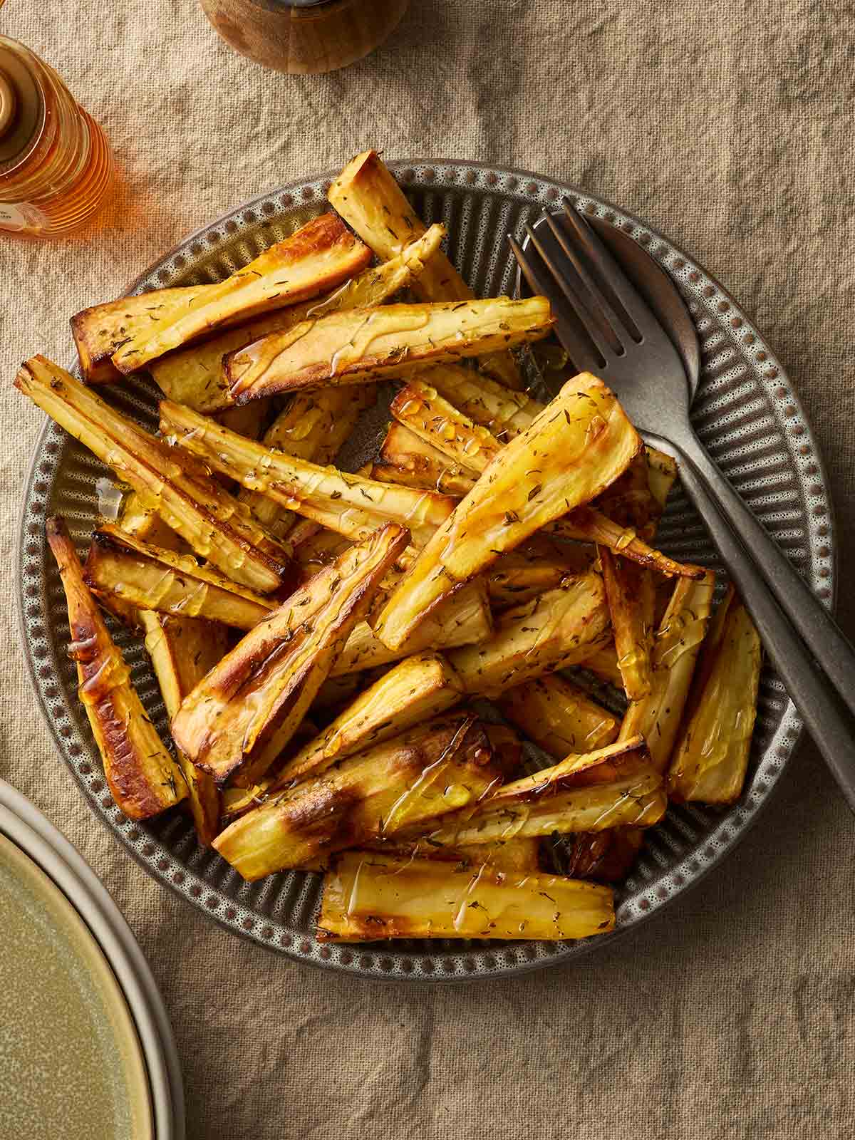 A bowl filled with roast parsnips with a fork and knife in.