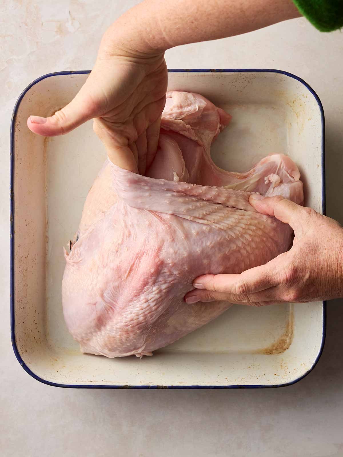 A hand inside the skin of a raw turkey, getting it ready to roast.