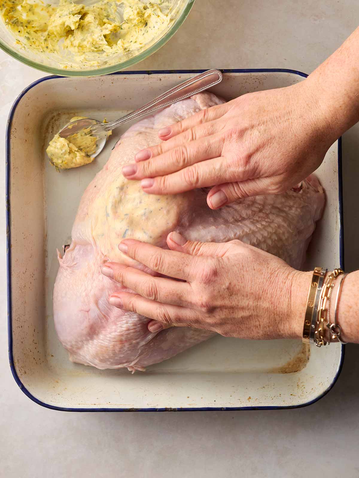 Two hands spreading butter that's under the skin of a raw turkey, getting it ready for roasting.