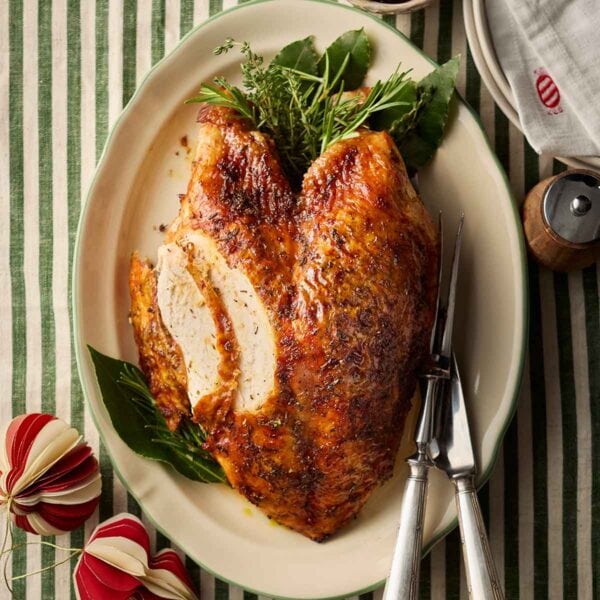A golden cooked turkey crown on a platter with two slices out of it, on a dressed table ready for Christmas.