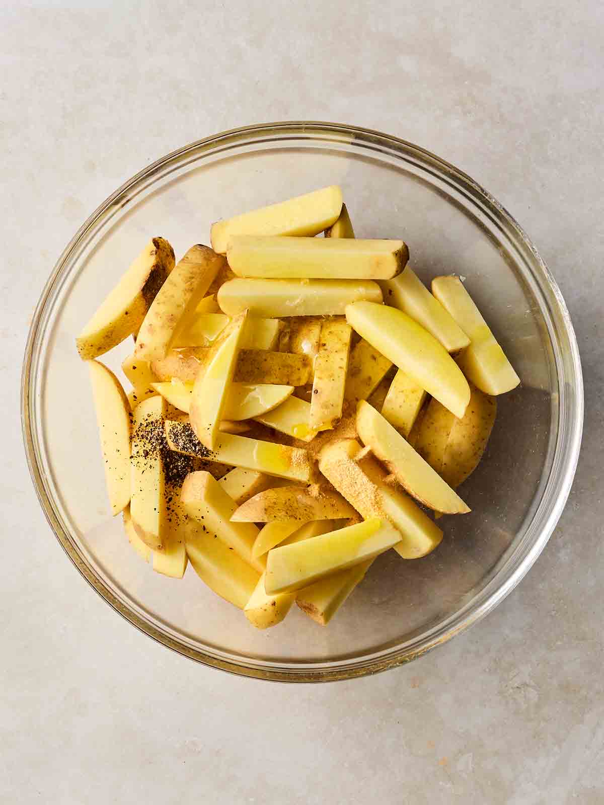 Potatoes cut up into chip shape in a glass bowl on a white surface.