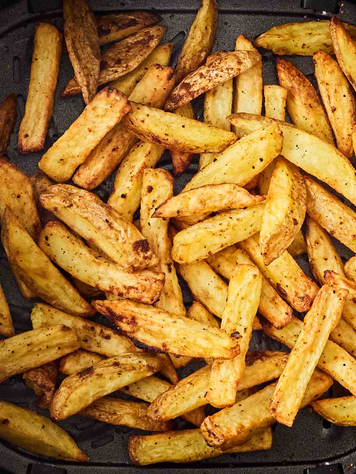 A close up of golden homemade chips in an air fryer pan.