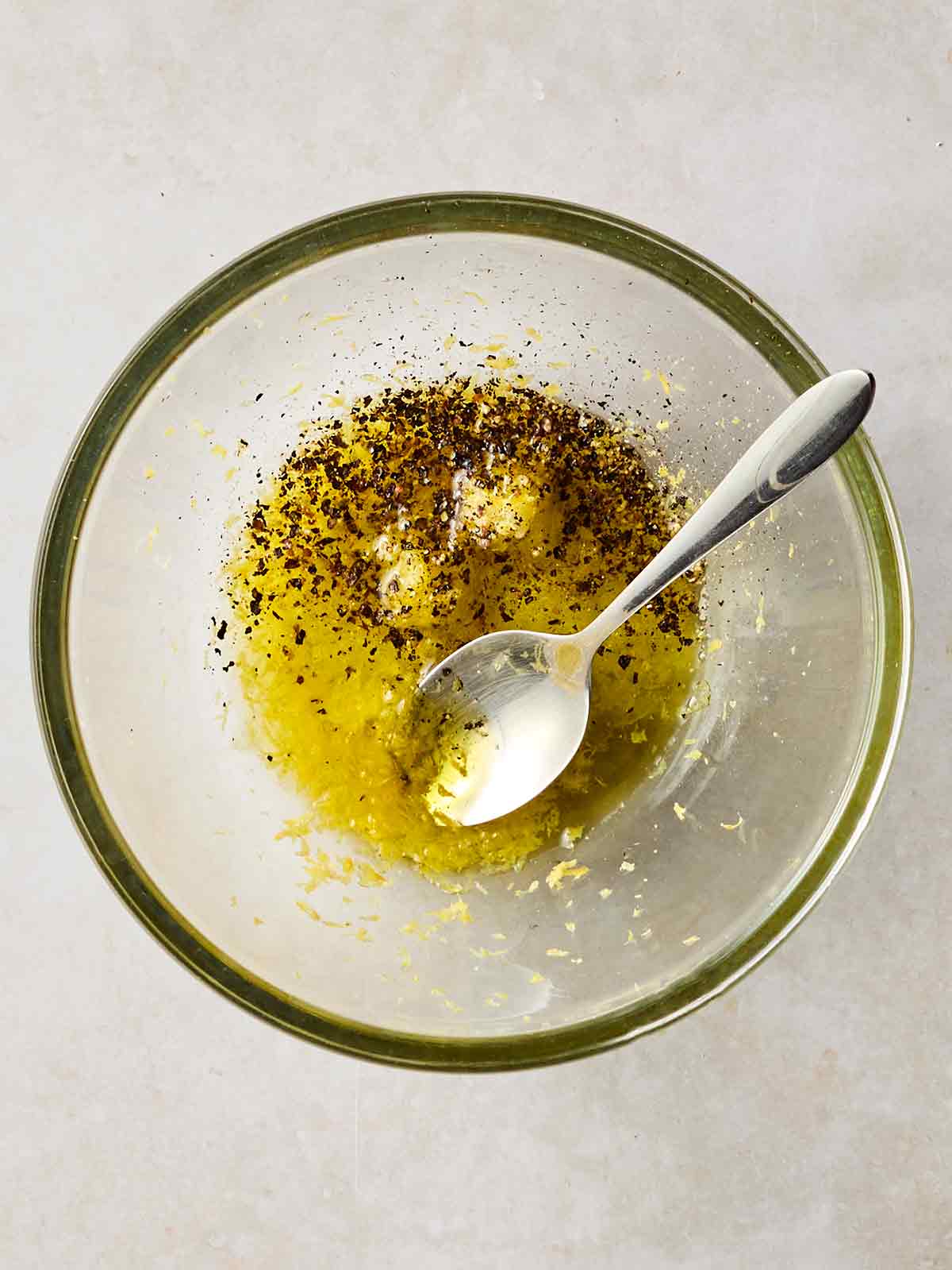 A glass bowl with a dressing inside, with olive oil, garlic, lemon juice and herbs.