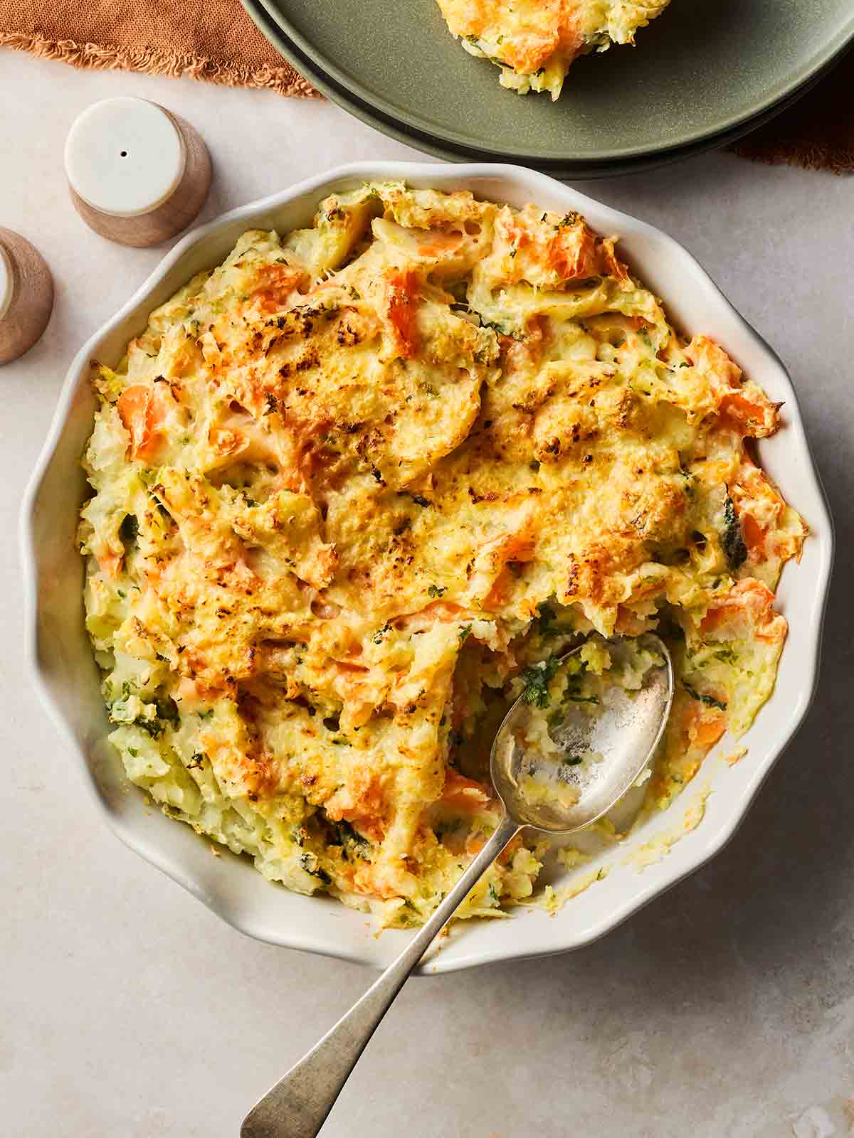 A bowl of Bubble and Squeak with a serving spoon inside with a portion missing.