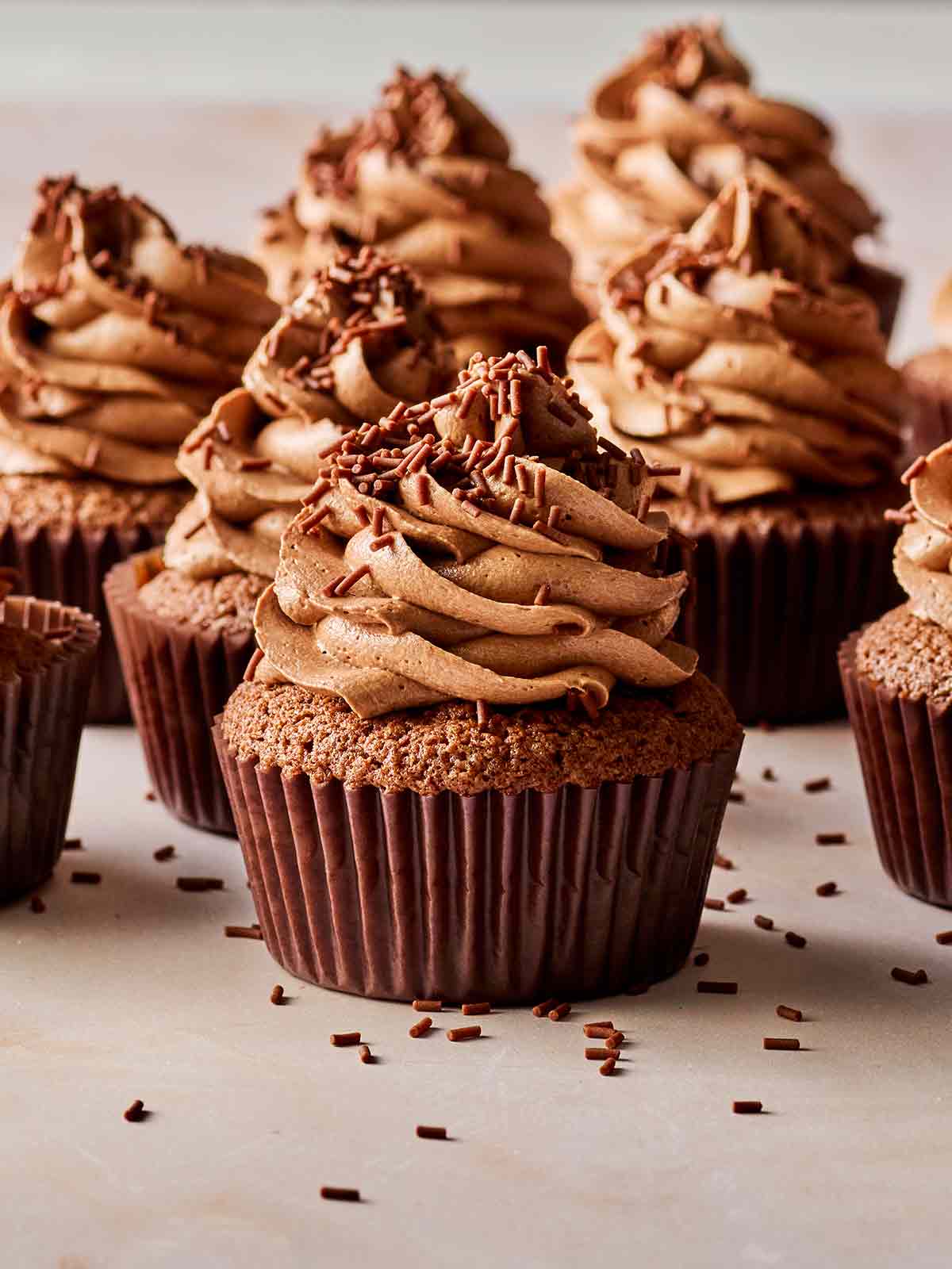 Easy chocolate cupcakes swirled with icing and sprinkles in brown cases.