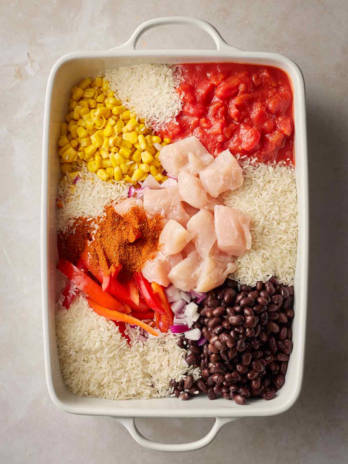 Chicken and other ingredients in a baking dish together, ready to cook, for a Dump and Bake Burrito Chicken Rice recipe.