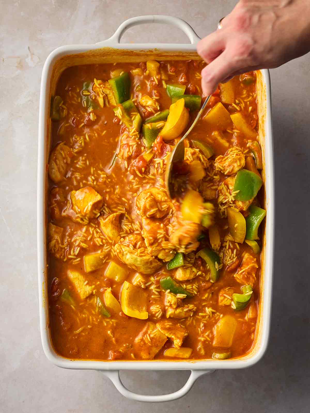 A hand stirring an oven dish with chicken curry and rice in.