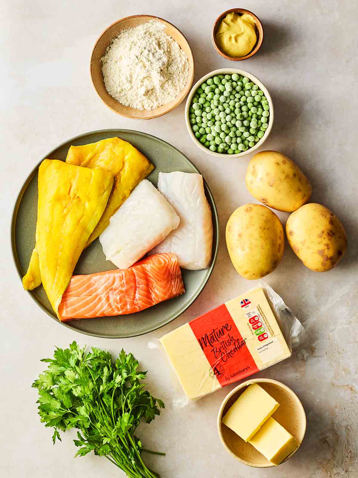 The raw ingredients for making a Fish Pie laid out on a white surface.