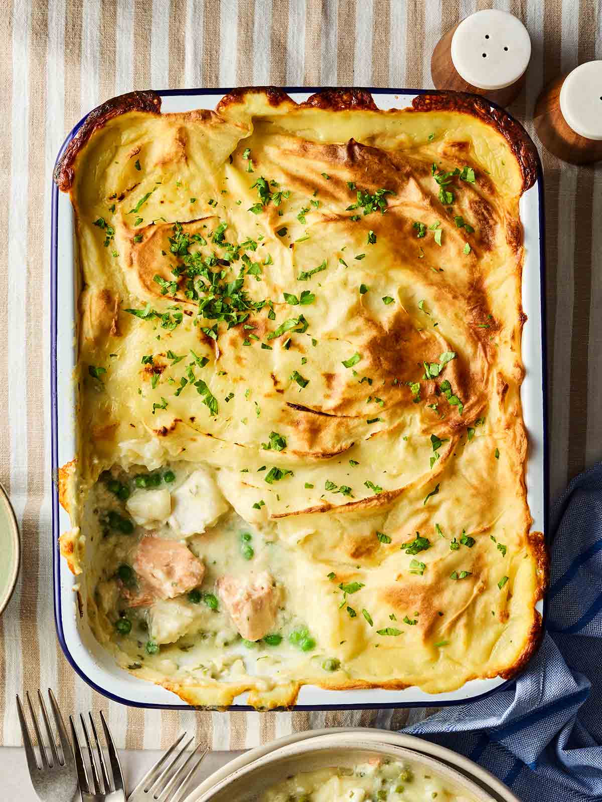 A cooked fish pie in an oven dish, on a table with a stripy tablecloth, ready to serve.
