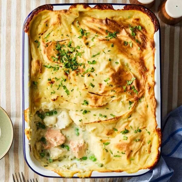 A bird's eye view of a Fish Pie, with a portion missing after being served. Showing the filling of chunky fish, peas and a creamy white sauce.