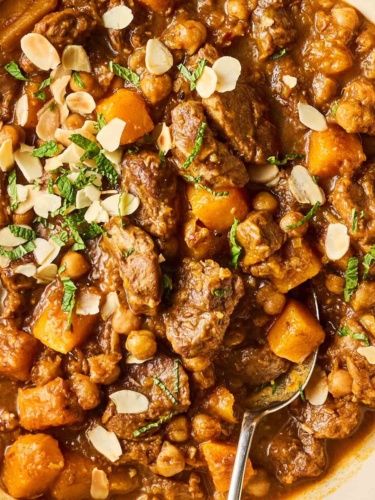 A close up of cooked ingredients in a pot, made up of lamb, butternut squash, chickpeas and almonds.