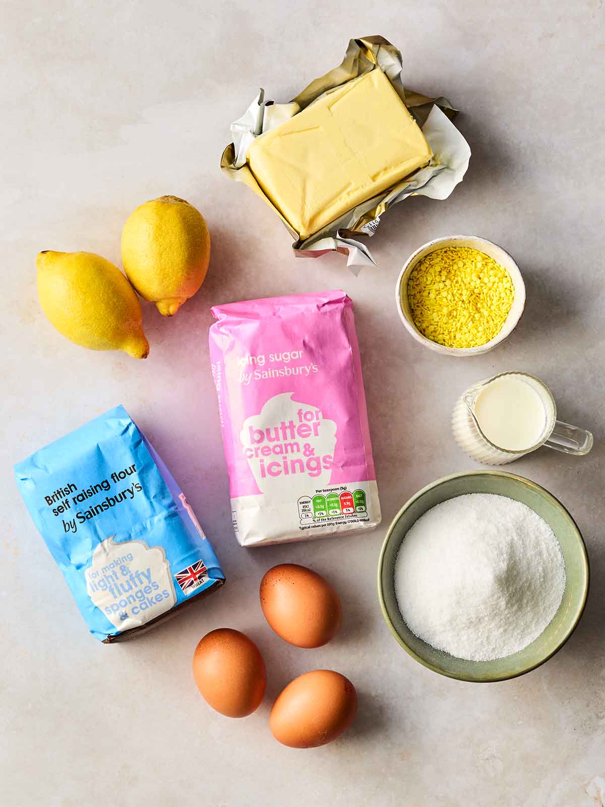 The raw ingredients for making Lemon Cupcakes laid out on a white work surface.
