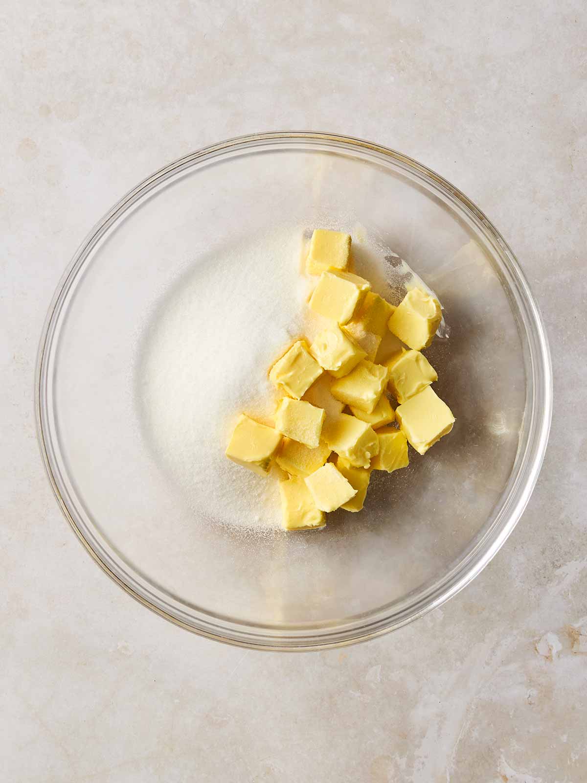 Cubes of butter and sugar in a glass bowl on a white surface.