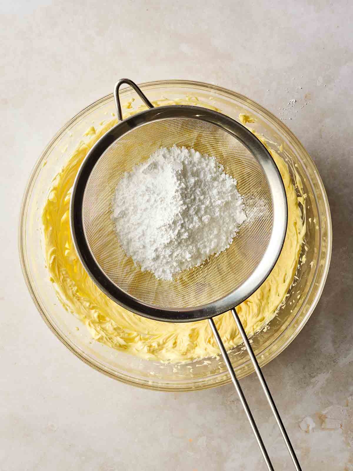 Icing sugar in a sieve, over a glass bowl of cake batter.