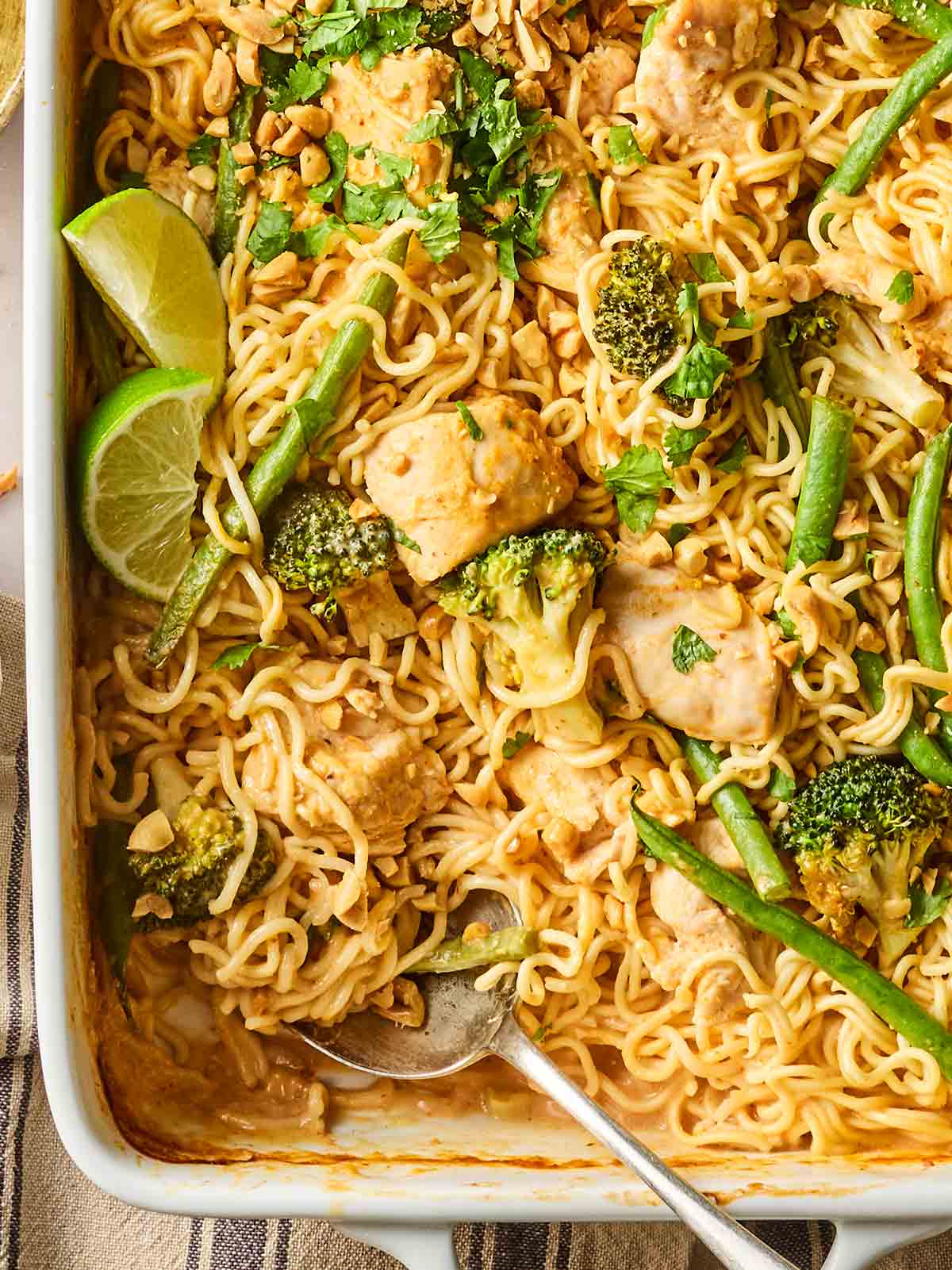 The edge of an oven dish with spicy peanut butter chicken noodles inside, with a spoon ready to serve.