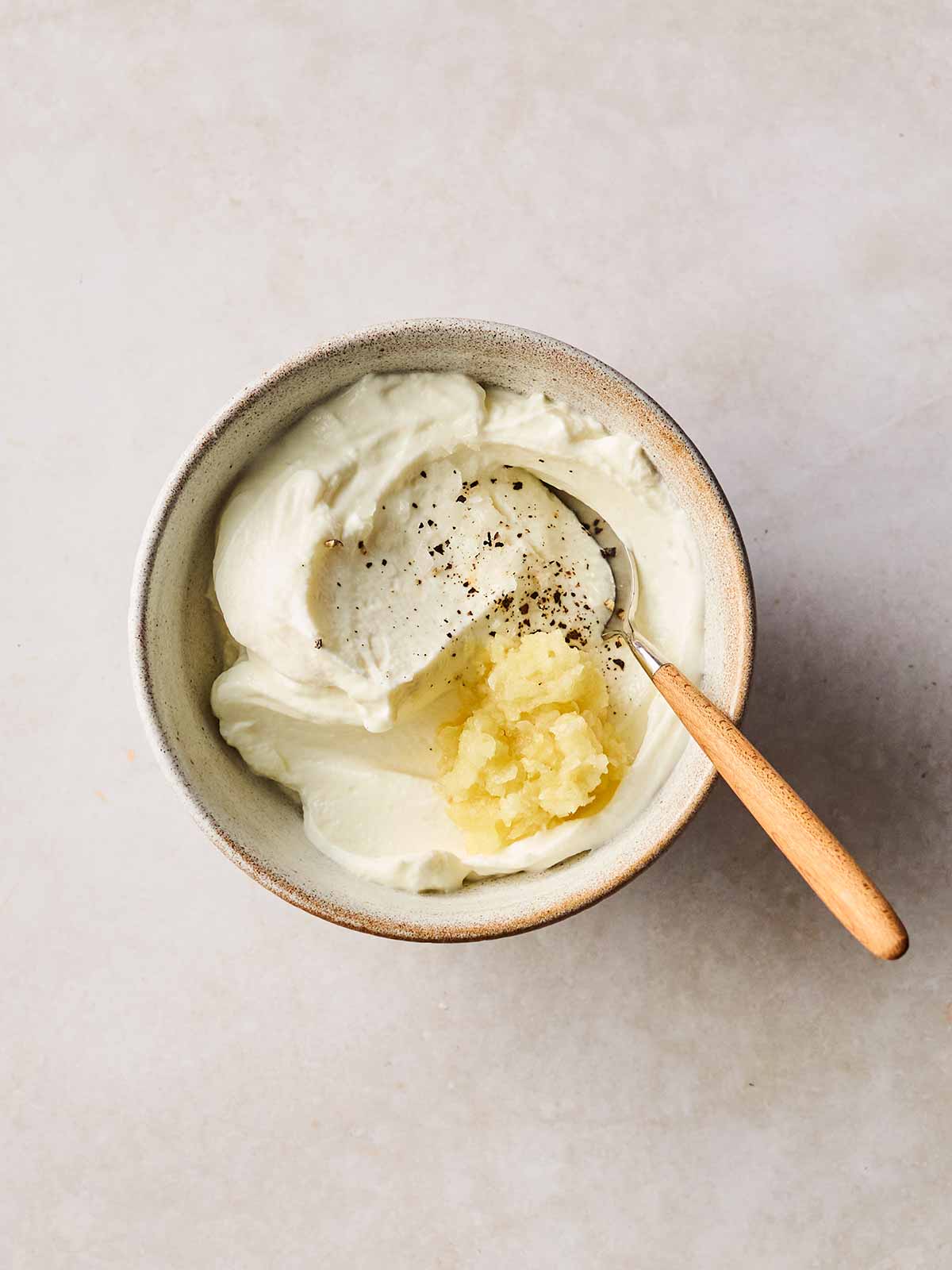 A dish with garlic and Greek yogurt inside, with a spoon to stir.