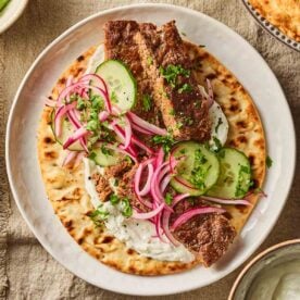 A close up of a sheet pan kebab, made up with salad and sauce and a flatbread underneath.