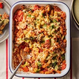 A big pan of baked tuna with pasta, cheese on top and vegetables, a portion having been served.