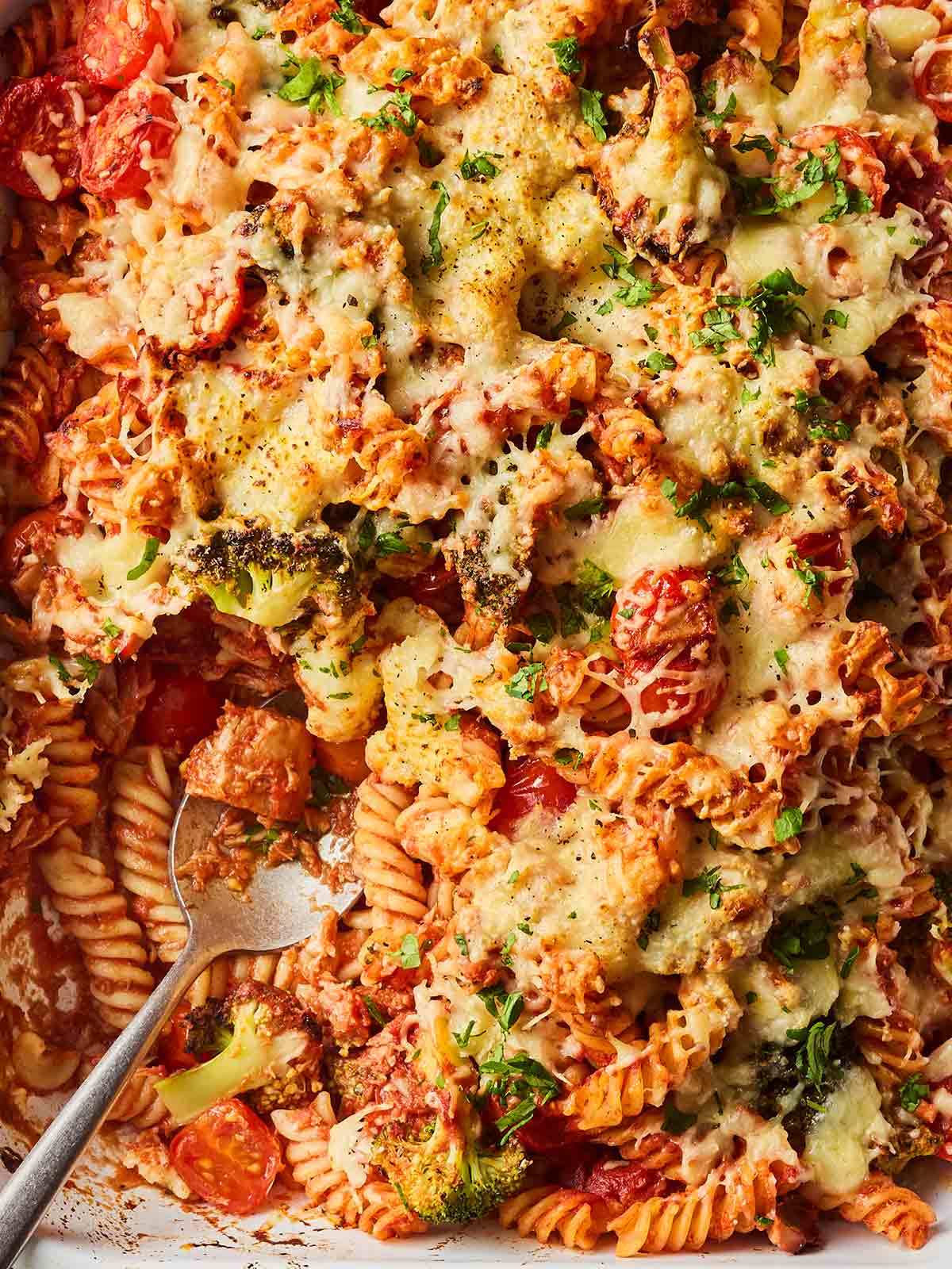 A close up of tuna pasta bake, with a spoon in the side and cheese on top.