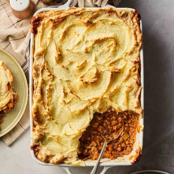 A vegetarian cottage pie straight out of the oven with a golden brown top and a portion already dished out with a spoon.