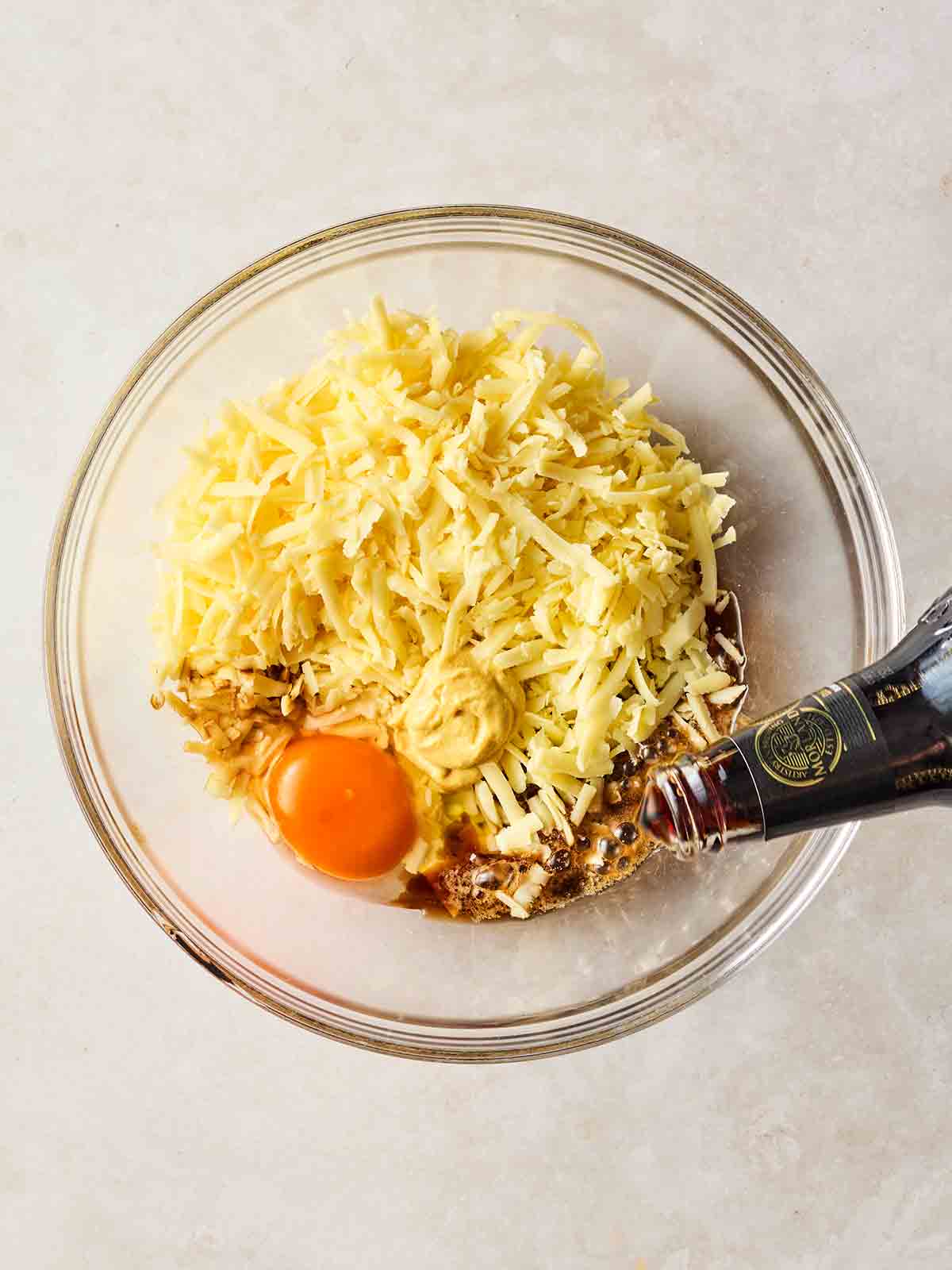 A glass bowl filled with grated cheese, an eggs and some beer being poured in.