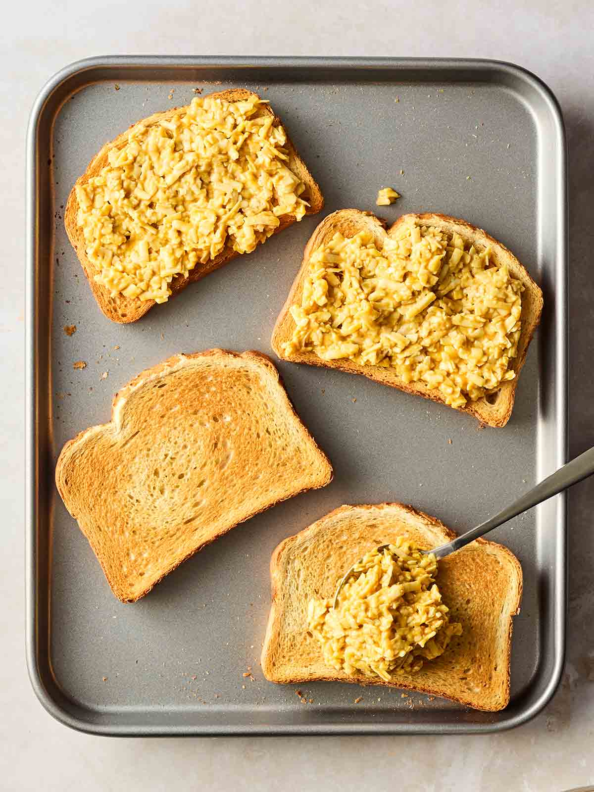 An oven tray with four slices of toasted bread on and a cheese mixture on top. Welsh Rarebit going into the oven.