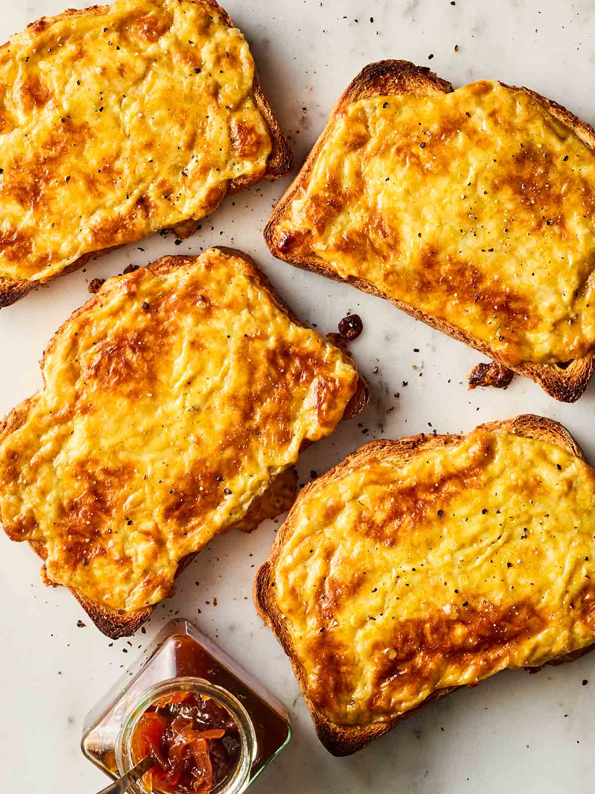 Four slices of Welsh rarebit with chutney on the side.