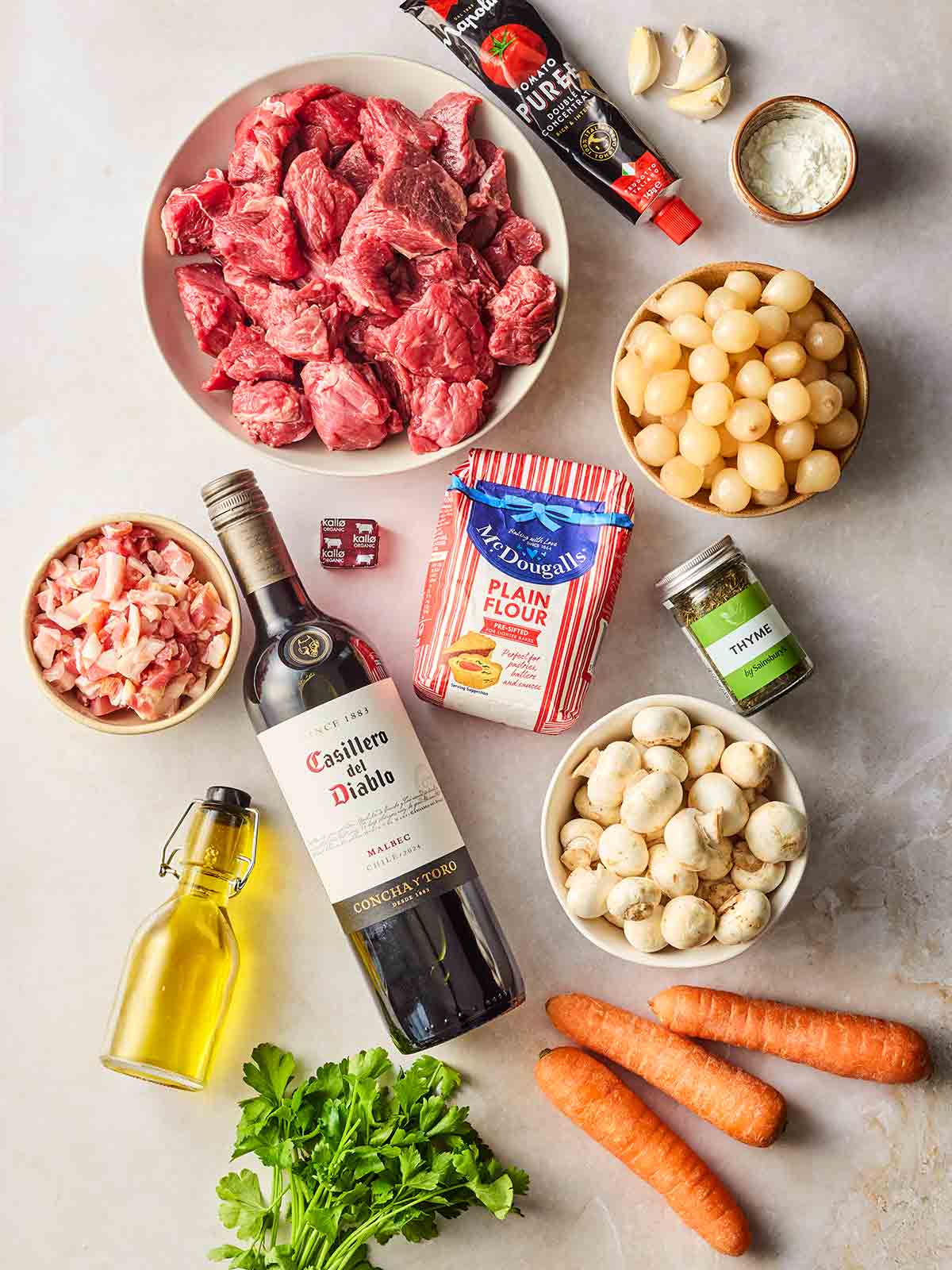 The ingredients for making beef bourguignon laid out on a white surface.