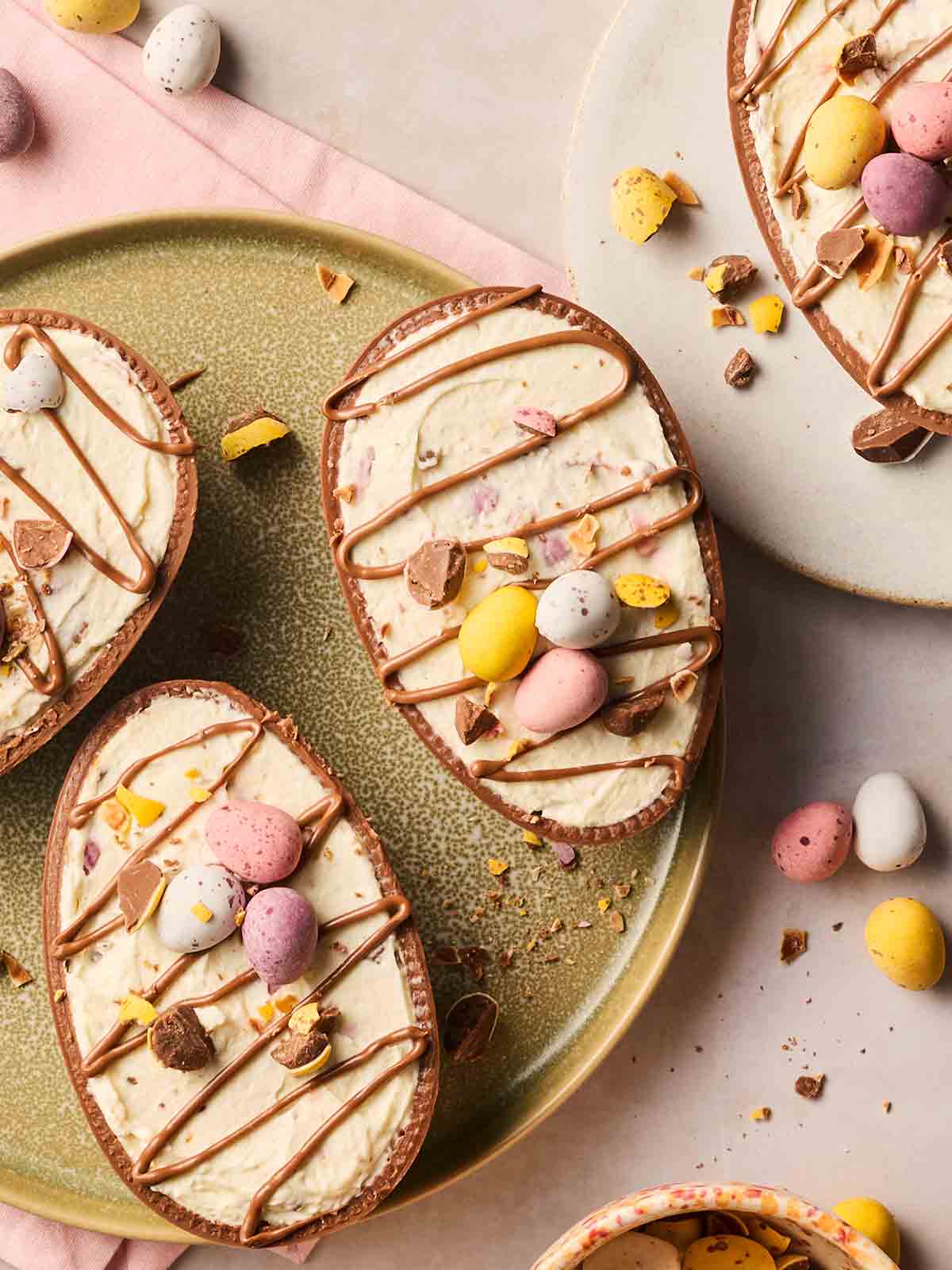 Four halves of Easter eggs on plates, each filled with cream for a modified Easter cheesecake.