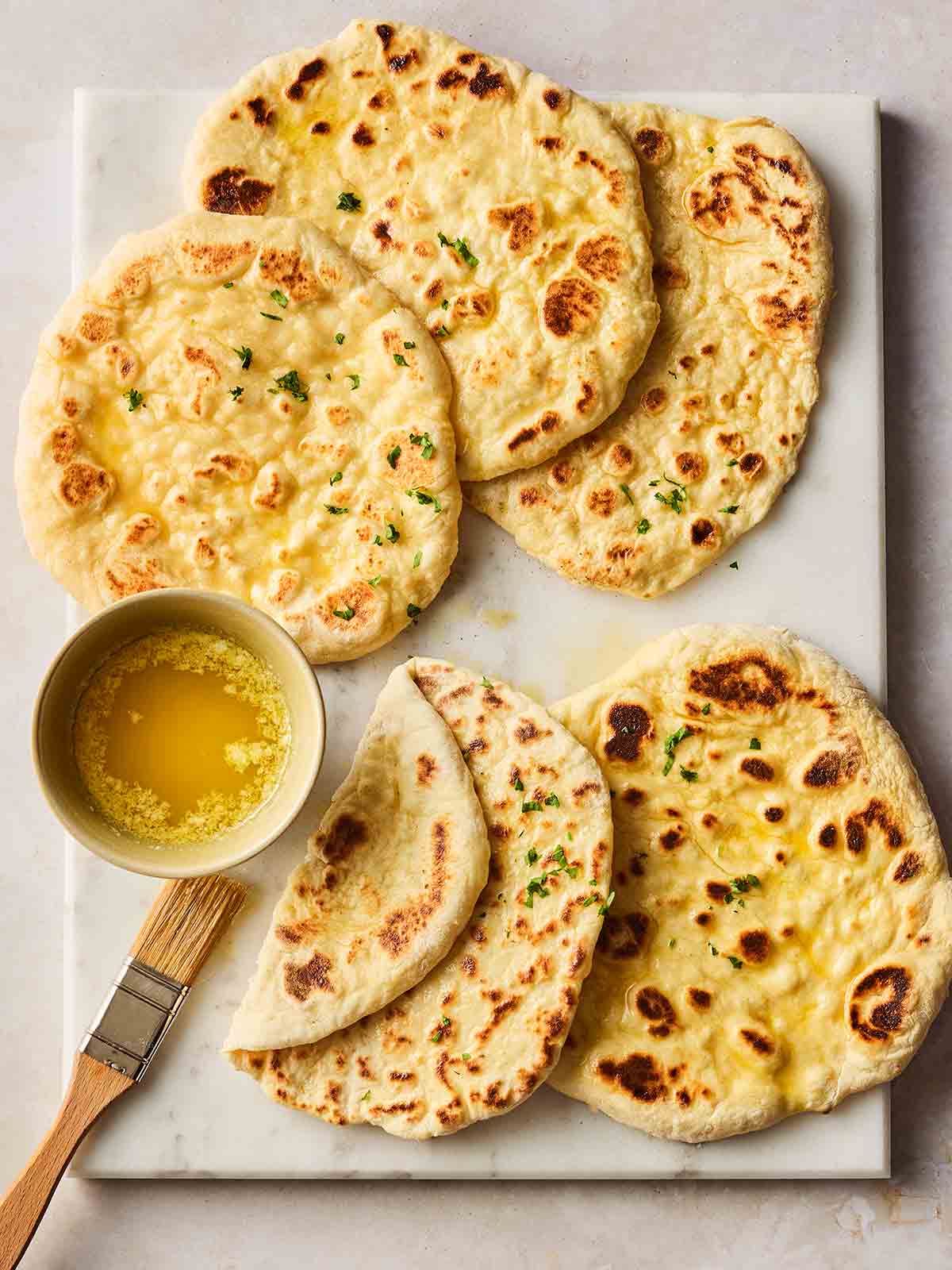 A white board with small, round, homemade flatbreads on, brushed with melted butter on the side.