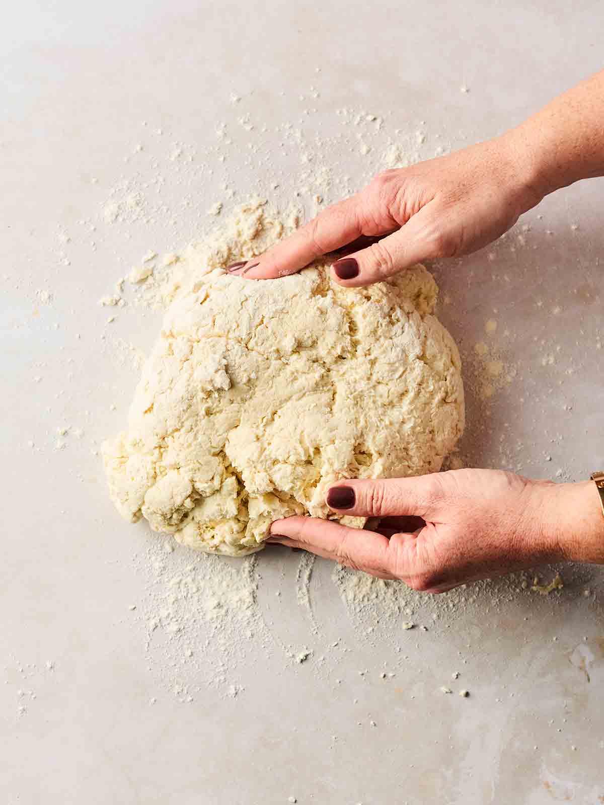 Two hands with a ball of flatbread dough in the middle of them, starting to knead.