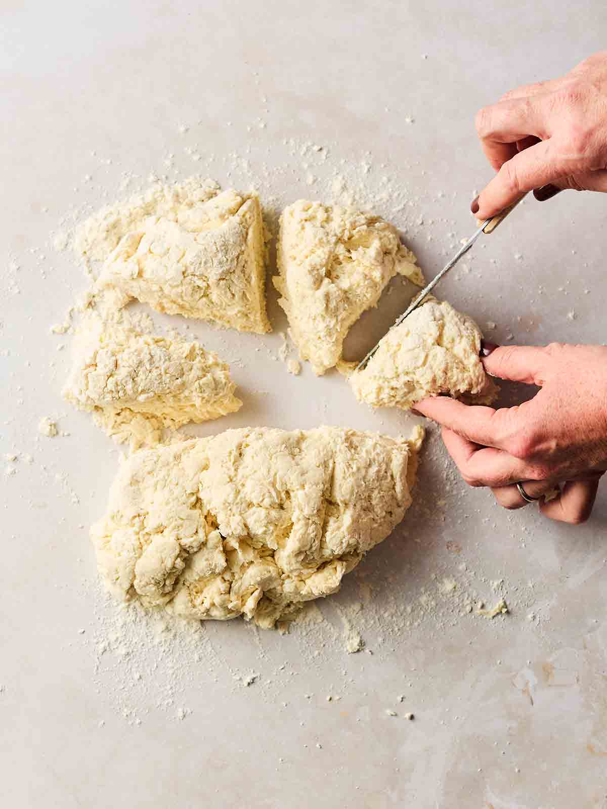 A ball of flatbread dough on a white surface, being cut into equal parts with a knife.