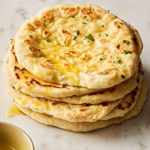 A tower of garlic flatbreads, small and round, on a surface.
