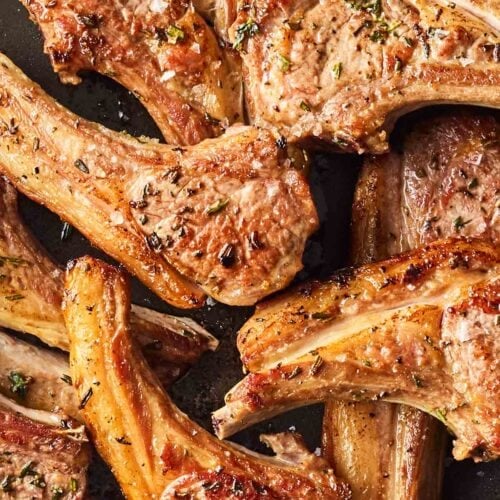 A pan filled with cooked lamb chops, seasoned with herbs, ready to eat.