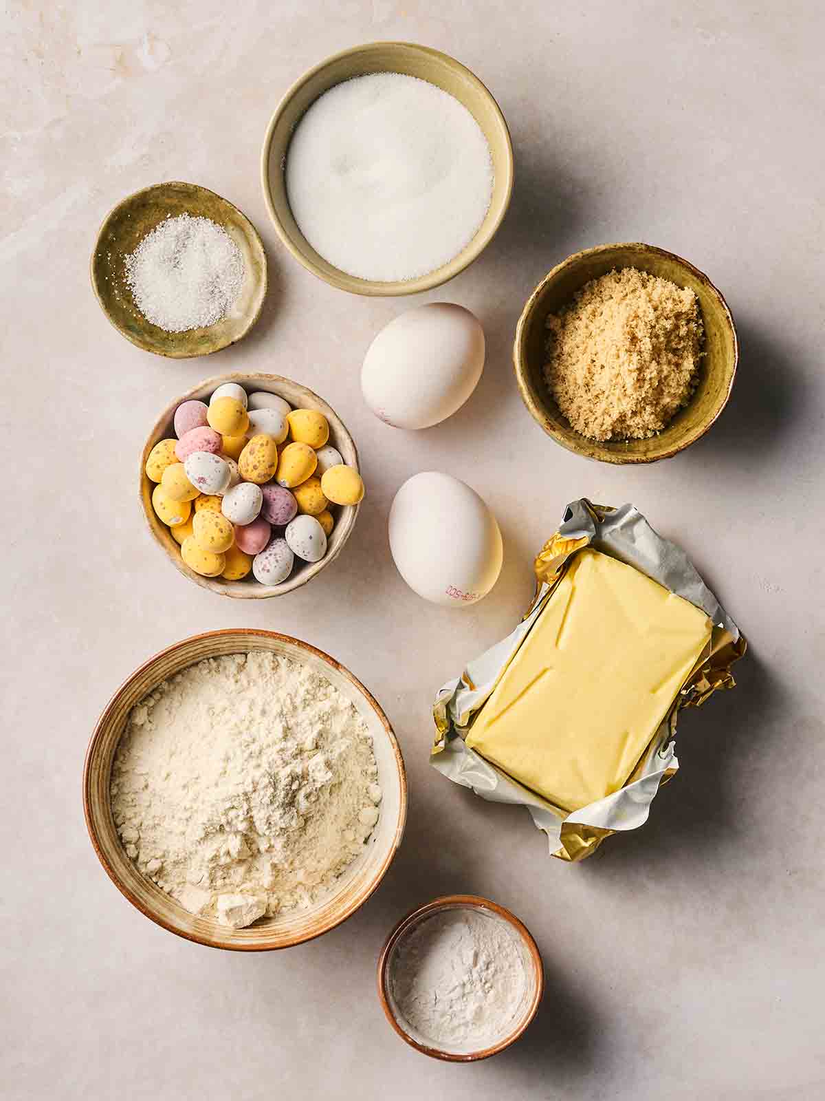 Bowls of ingredients for baking Mini Eggs Cookies on a white surface.