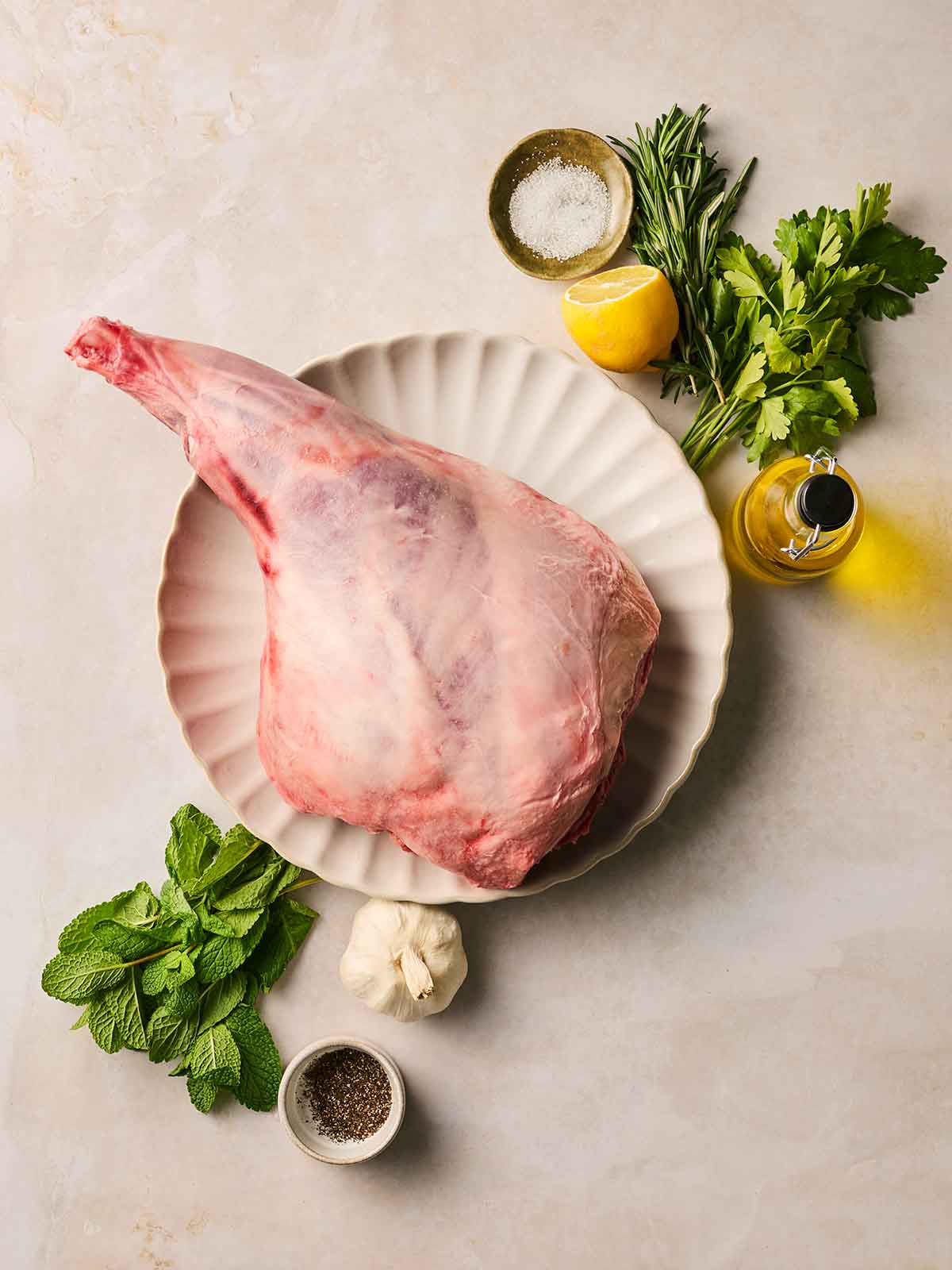 The ingredients for making a roast leg of lamb laid out on a white counter top.
