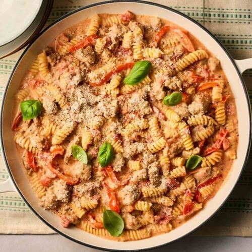 A pan of one pot Sausage Pasta with cheese and basil over the top. On a table, ready to dish out.