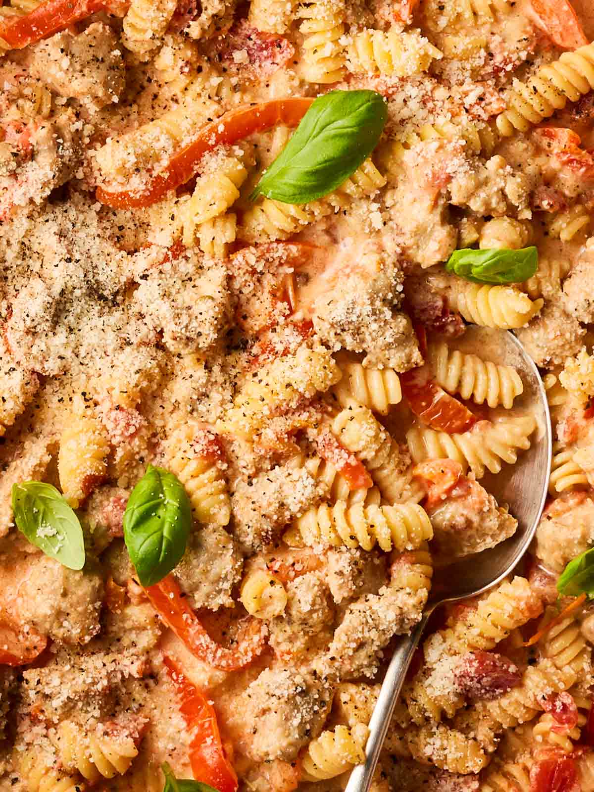 A close up of a pasta dish, mixed in a tomatoey sauce with sausage balls, peppers, basil, and parmesan.
