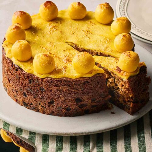 A classic Simnel Cake, made with fruit and marzipan, on a plate with a slice already cut.
