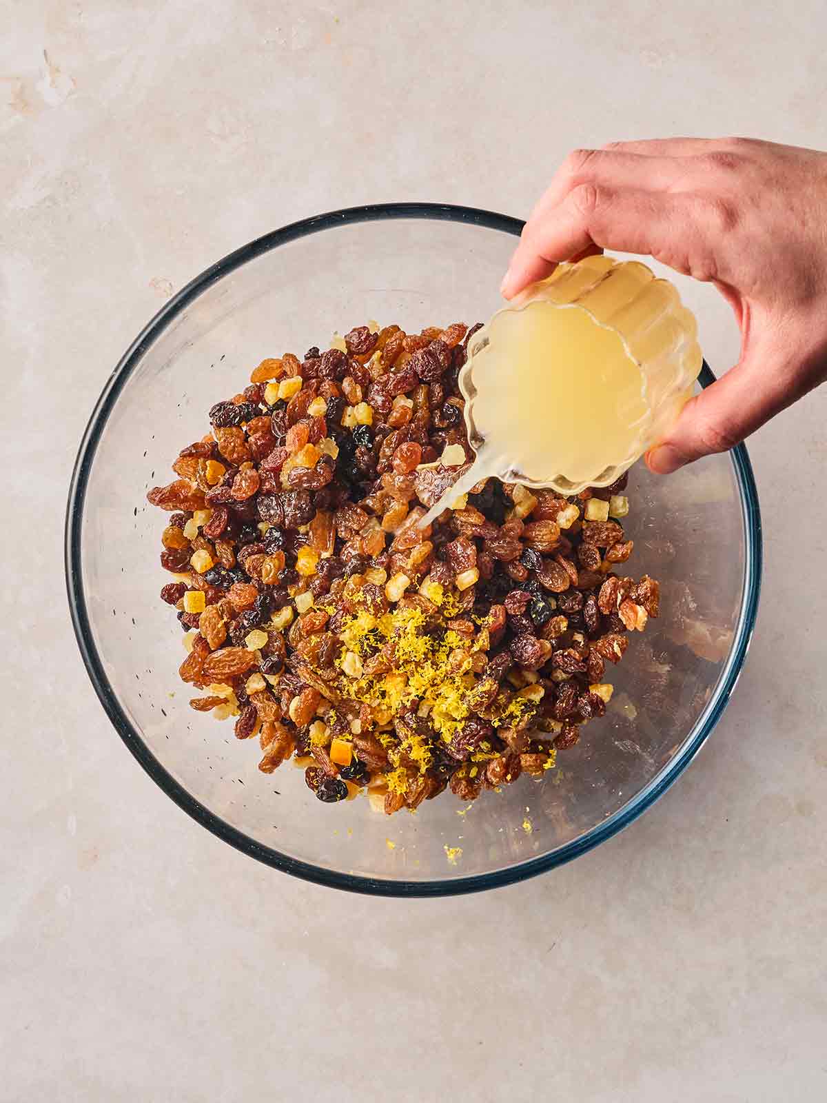 A glass bowl of dried fruit, with a hand pouring in apple juice to soak.