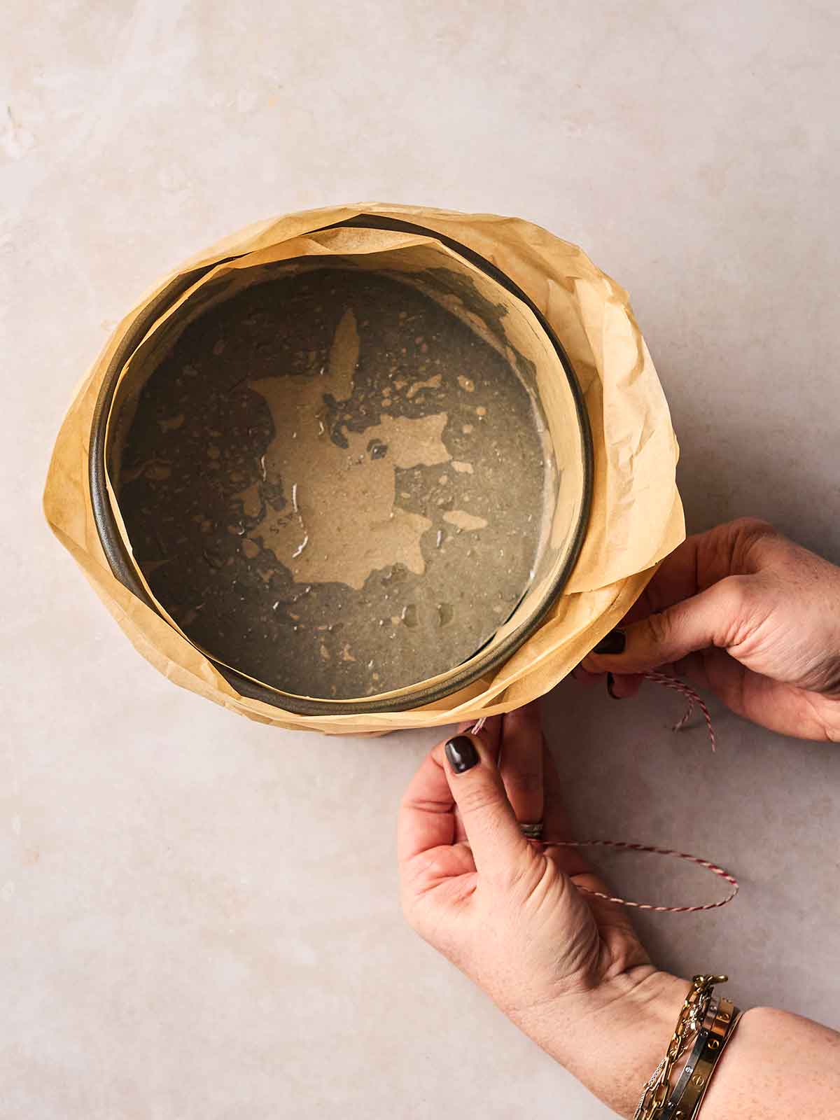 Two hands lining a cake tin with baking paper and string.