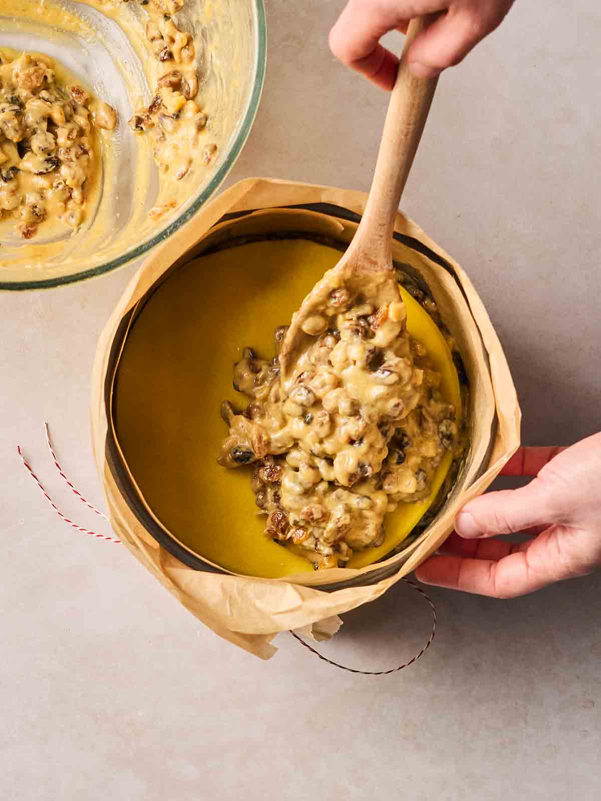 Half of a fruit cake mixture being spooned into a cake tin on top of marzipan.