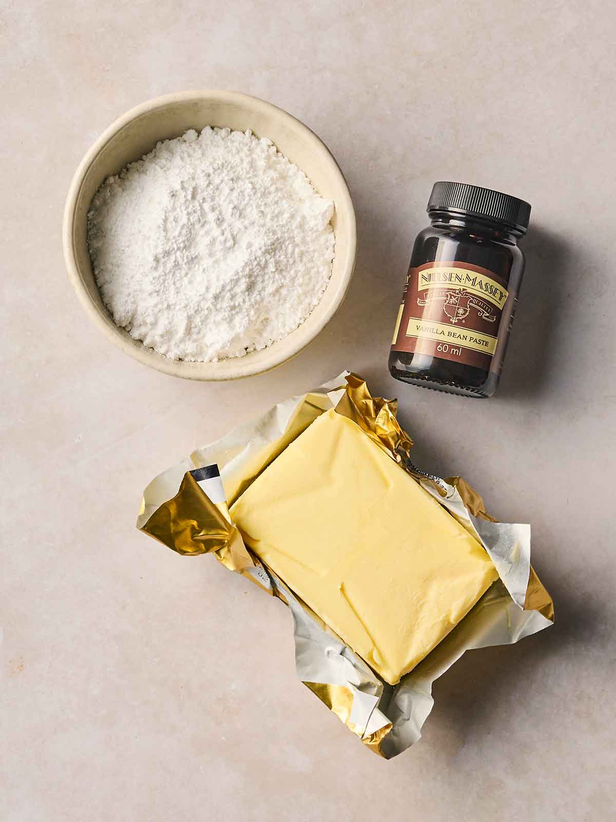 The ingredients for making buttercream icing laid out on a counter, including butter, icing sugar and vanilla.