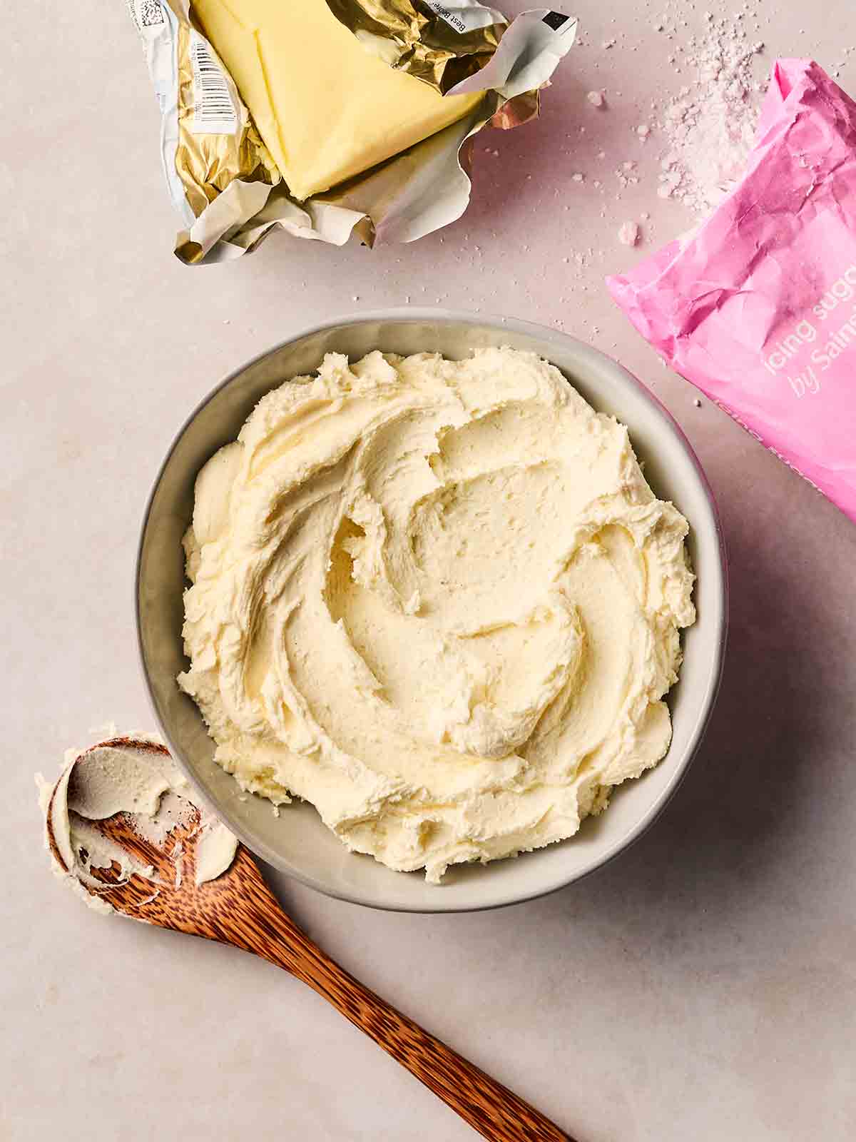 A bowl of fresh buttercream icing with a spoon to the side.