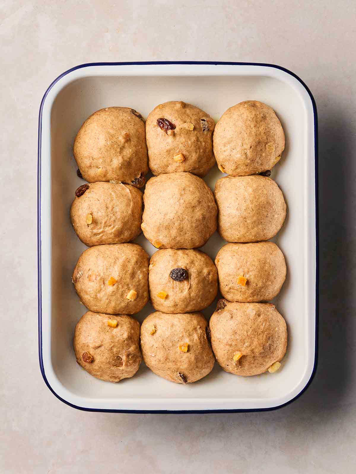 A white oven dish with 12 ready-to-bake but undecorated hot cross buns inside.